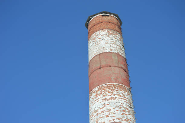 Red and white round brick chimney of a boiler room against a blue sky.