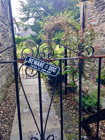 A gate to a cute house with the sign “Beware of the Dog, Enter at Own Risk”