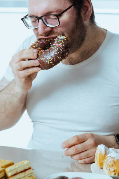 istock Man with excess weight eat chocolate donut 2027366750