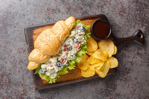 Homemade Healthy Chicken Salad Croissant Sandwich with potato chips closeup on a wooden board on the table. Horizontal top view from above
