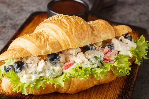 Chicken salad on a flaky butter croissant on a wooden board on the table. Horizontal