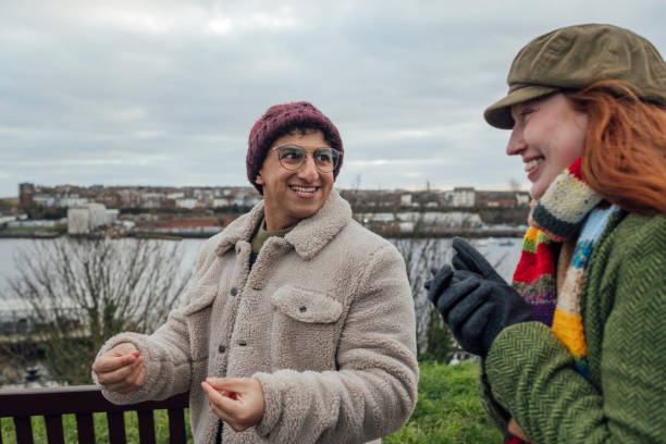 Two young men in casual hoodies sitting on a park bench outdoors, enjoying a relaxed conversation during an autumn day