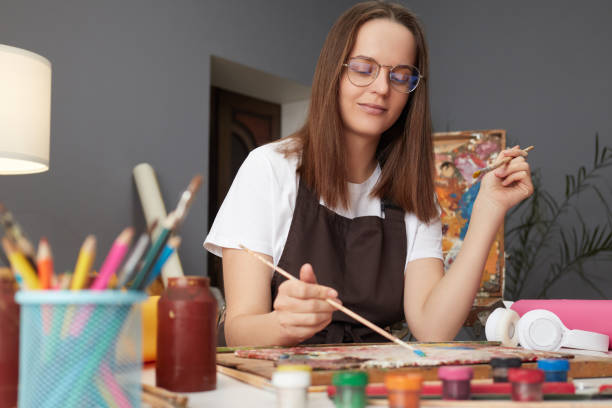 istock Artistic talent workshop. Painter's creative studio. Artwork inspiration session. Caucasian woman painter wearing brown apron in art studio drawing picture 2027403769
