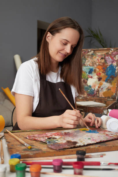 istock Drawing inspiration from nature. Studio palette for vibrant paintings. Satisfied delighted Caucasian woman painter wearing brown apron in art studio drawing picture enjoying her hobby 2027403782