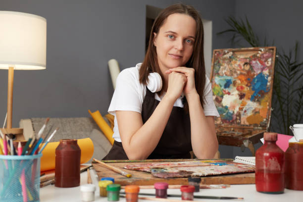istock Watercolor artwork in studio. Creative education for aspiring artists. Charming kind Caucasian woman wearing brown apron painting in art creative studio 2027404268