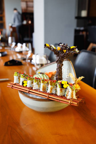 Sushi rolls lined up on bamboo mat on top of bowl with crushed ice served on table in fine dining
