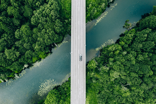 Aerial view of bridge road with car over blue river and green summer woods in Finland