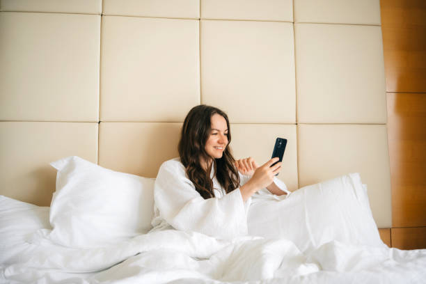 istock Smiling happy woman relaxing in bed and using smartphone 2027457401