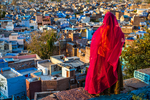 Young Indian woman looking at the view. The Blue City of Jodhpur on the background. Jodhpur is known as the Blue City due to the vivid blue-painted houses around the Mehrangarh Fort.