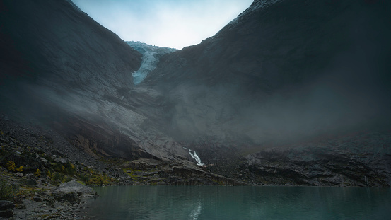 Norwegian mountain landscape, cloudy, with a lake, with the tongue of the Briksdalsbreen glacier in the background, over the snow-capped mountains.