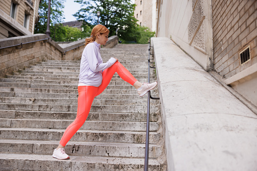 Beautiful mid adult woman taking up outdoor exercise, stretching legs on stone staircase in Paris, city life new beginnings