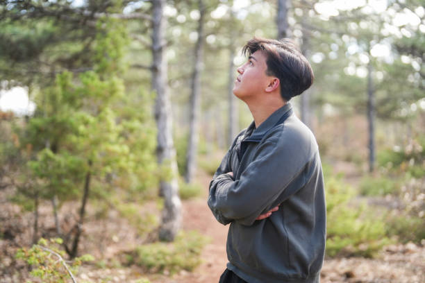 young man standing in front of pine trees in the forest looking at nature