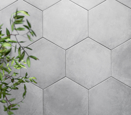 Background of gray hexagon shaped ceramic tiles with green branches. Trendy empty backdrop for displaying products or advertising. Top view and copy space.