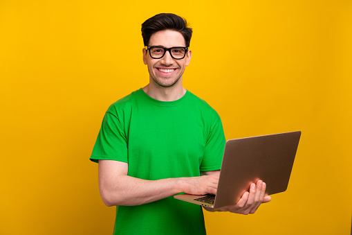 Photo of young happy guy positive business developer analytic wear eyeglasses holding modern netbook isolated on yellow color background.