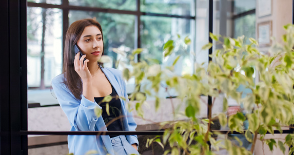 Beautiful businesswoman in an office talking on phone crossing hands and looking at camera with a smile.