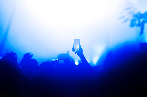 Silhouette of a hand holding a smartphone capturing a moment during a night concert lit by stage lights