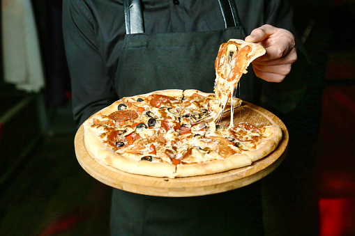 A professional chef wearing an apron holds a freshly baked pizza with a variety of toppings.