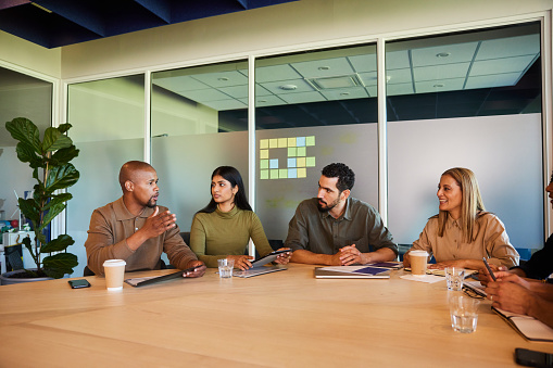 Young businessman talking with a diverse group of colleagues during a meeting together around a board room table in an office