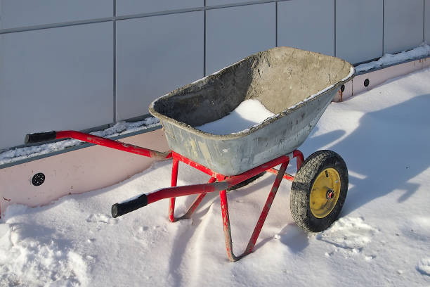 a two-wheeled wheelbarrow in the snow near a building under construction.