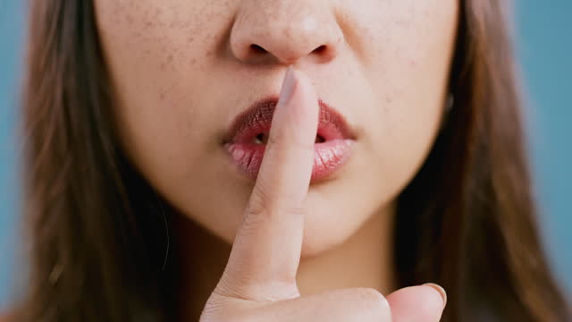 Closeup, woman and studio with lips in secret for noise, privacy and confidential information with finger sign. Person, emoji and quiet for mystery and silence with hand gesture on blue background