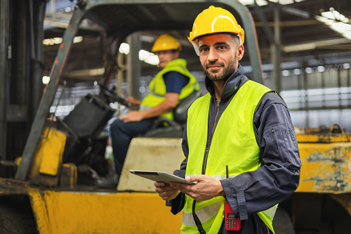 Warehouse workers wear helmets Surrounded by industrial and construction elements. Demonstrate safety, hard work and use tablet to check machine data