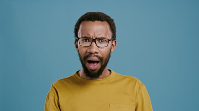 Face, surprise and black man in glasses with shock for announcement in studio isolated on a blue background mockup space. Portrait, wow and amazed African person with bad news, information and angry
