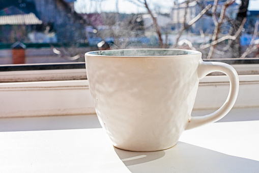 cup of hot drink with tea or coffee stands on the sill near the window. Day off