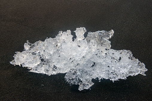 Delicate piece of Ice washed up on the ash  beach also known known as Jokulsarlon diamond Beach near the glacier lagoon of Jokulsarlon, Iceland during sunrise over the Atlantic Ocean.