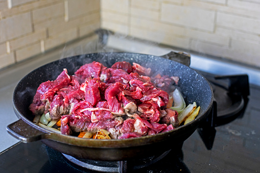 raw fresh meat cut into pieces in a frying pan. Cooking at home in the kitchen