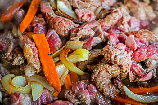 cook raw fresh meat cut into pieces in a frying pan with vegetables, top view