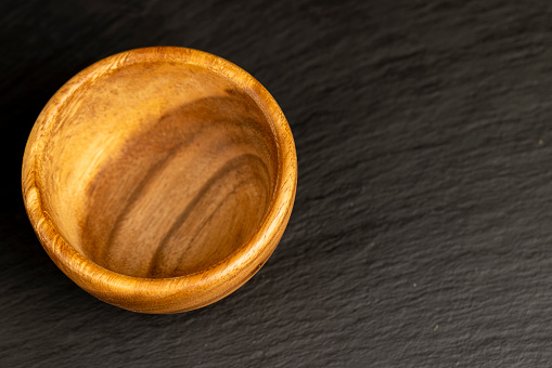 an empty wooden bowl on a black slate table, a black background and a wooden food bowl