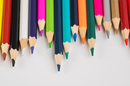 LONG WOODEN PENCILS OF VARIOUS COLORS, ON LIGHT WOODEN TABLE. HORIZONTAL PHOTOGRAPHY. COLOR.