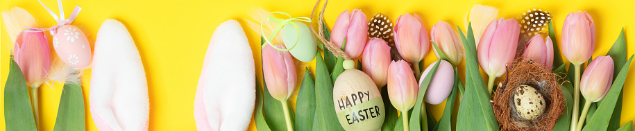 Easter composition with Plushy bunny ears,  eggs and spring flowers o on bright background top view flat lay