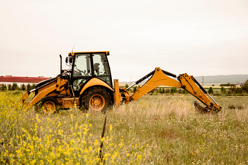 Tractor excavator against the background of spring flowers in the field. Preparing fields for sowing.