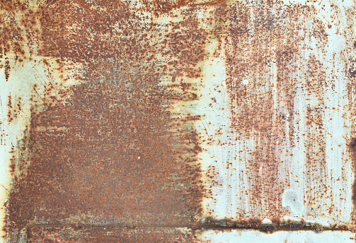 An old pitted and weathered rusty metal sheet background framed by old rusty bolts. Lots of texture with subtle abstract colors of the patina.