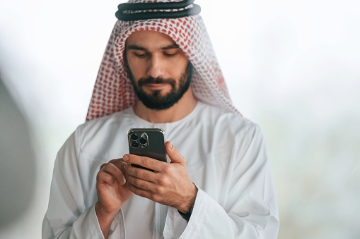 With smartphone in hand. Successful Muslim businessman in traditional outfit in his office.