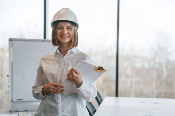istock Documents in hands. Young woman architect in hard hat is in office 2027738713