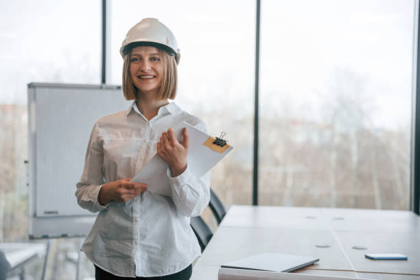 istock Documents in hands. Young woman architect in hard hat is in office 2027738717