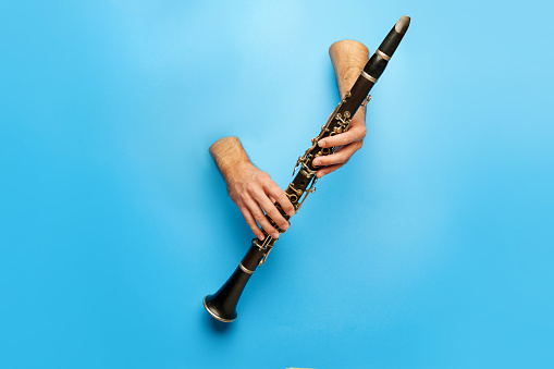 Male hands sticking out blue background with clarinet. Music therapy sessions advertisement for stress relief and relaxation. Concept of music, instruments, art, hobby, festival, performance