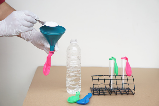 Closeup hands wears gloves holds funnel and flat pink balloon, put spoon of baking soda powder to pour into balloon. Concept, science experiment about reaction of chemical substance .