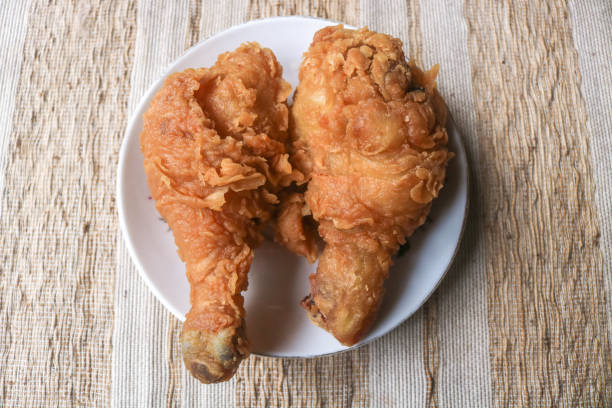 Two crispy fried chicken thighs on a white plate on a wooden table. Crypse flour fried chicken