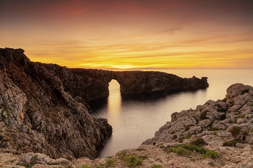 A view of the landmark stone arch of Pont d'en Gil on Menorca Island at sunset