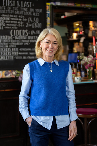 Three-quarter-length portrait of a mature woman smiling, looking into the camera. She is wearing smart casual attire. The bar/restaurant is located in Hexham.