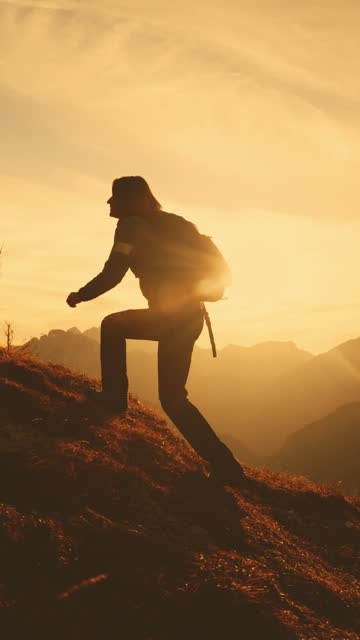 SLO MO Silhouetted Summit: Lone Female Trekker Ascending Grassy Mountain Slopes at Dusk
