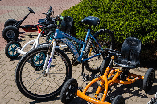 Parking for children's four-wheeled and adult two-wheeled bicycles on embankment, or Primorsky Boulevard in Arkhipo-Osipovka. Evergreens in background. Close-up. Gelendzhik, Russia - May 15, 2021
