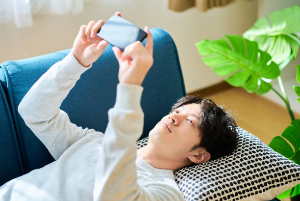 istock Young man lying on a sofa bed holding a smartphone 2027776390