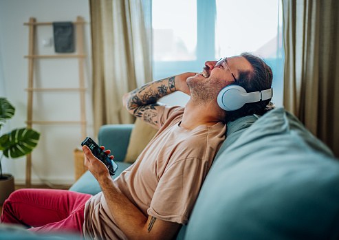 Cheerful young man relaxing while listening to music on headphones at home