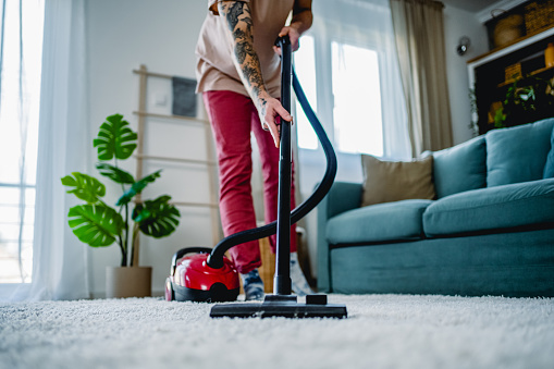 Young man cleaning a carpet with a vacuum cleaner at home