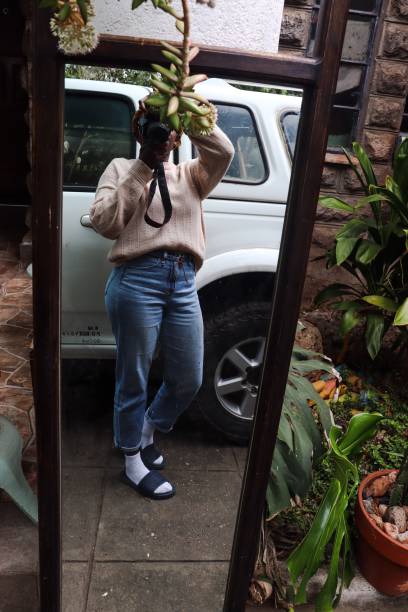 A young  black woman  taking  a mirror selfie with a camera outdoors