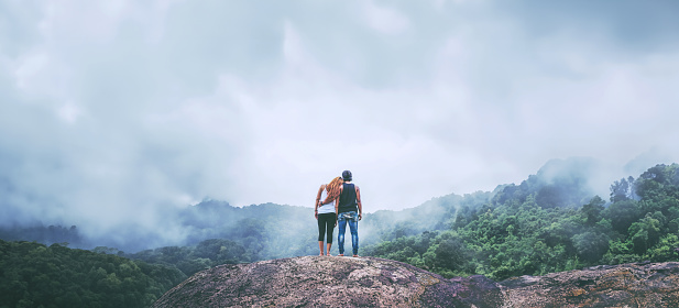 Lover women and men asians travel relax in the holiday. Standing hugged on a rocky cliff. Wild nature wood on the mountain.